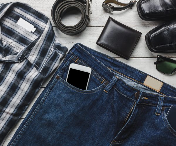 Top view accessories to travel with man clothing concept.Gentlemen items shirt,jean,mobile phone on wooden background and essentials wallet,belt,watch,sunglasses and leather shoes on wood table.